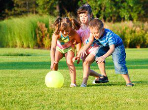 three kids playing with a ball on a manicured lawn